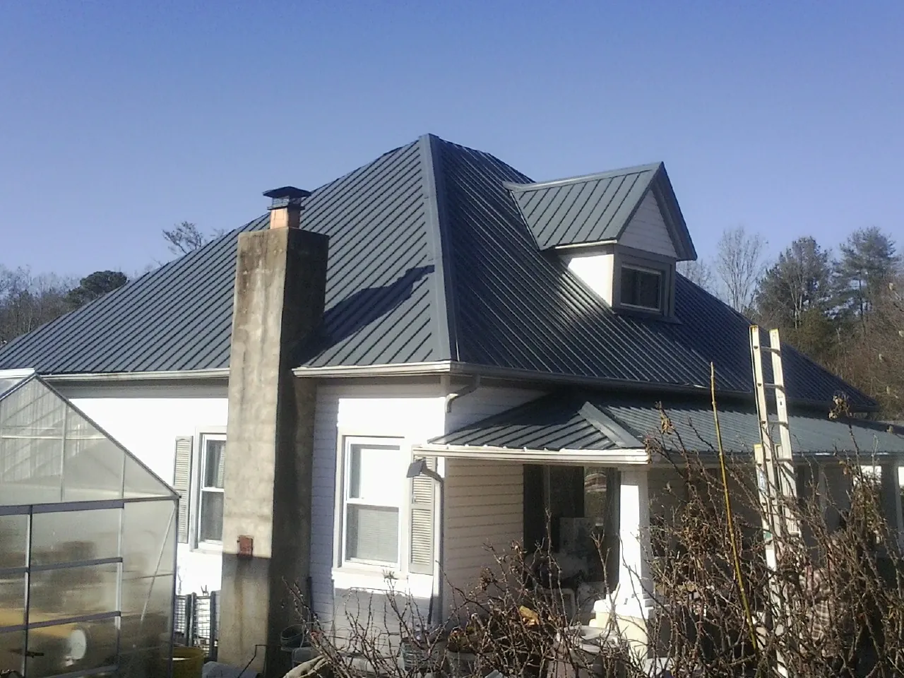 Dark blue standing seam metal roof on a white farmhouse with dormer — Slate & Tile Roof Repair by Roofing Brothers in Saint John