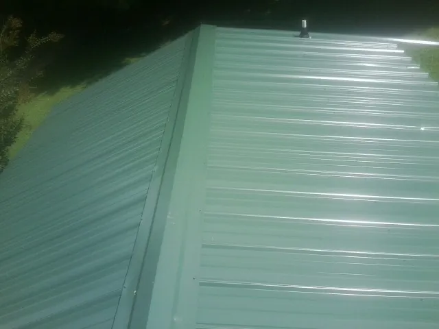New green metal panels meeting at the ridge of a roof — Flat Roof Repair work by our crew in Saint John