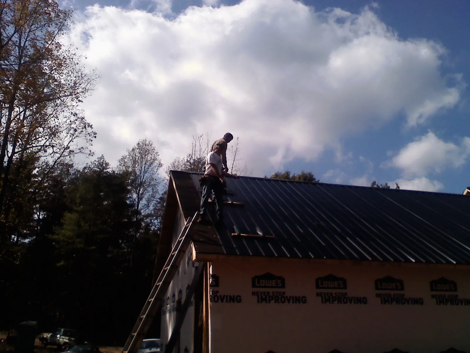 Roofer fastening dark metal panels high against a cloudy sky, from a Roof Inspection job in Saint John