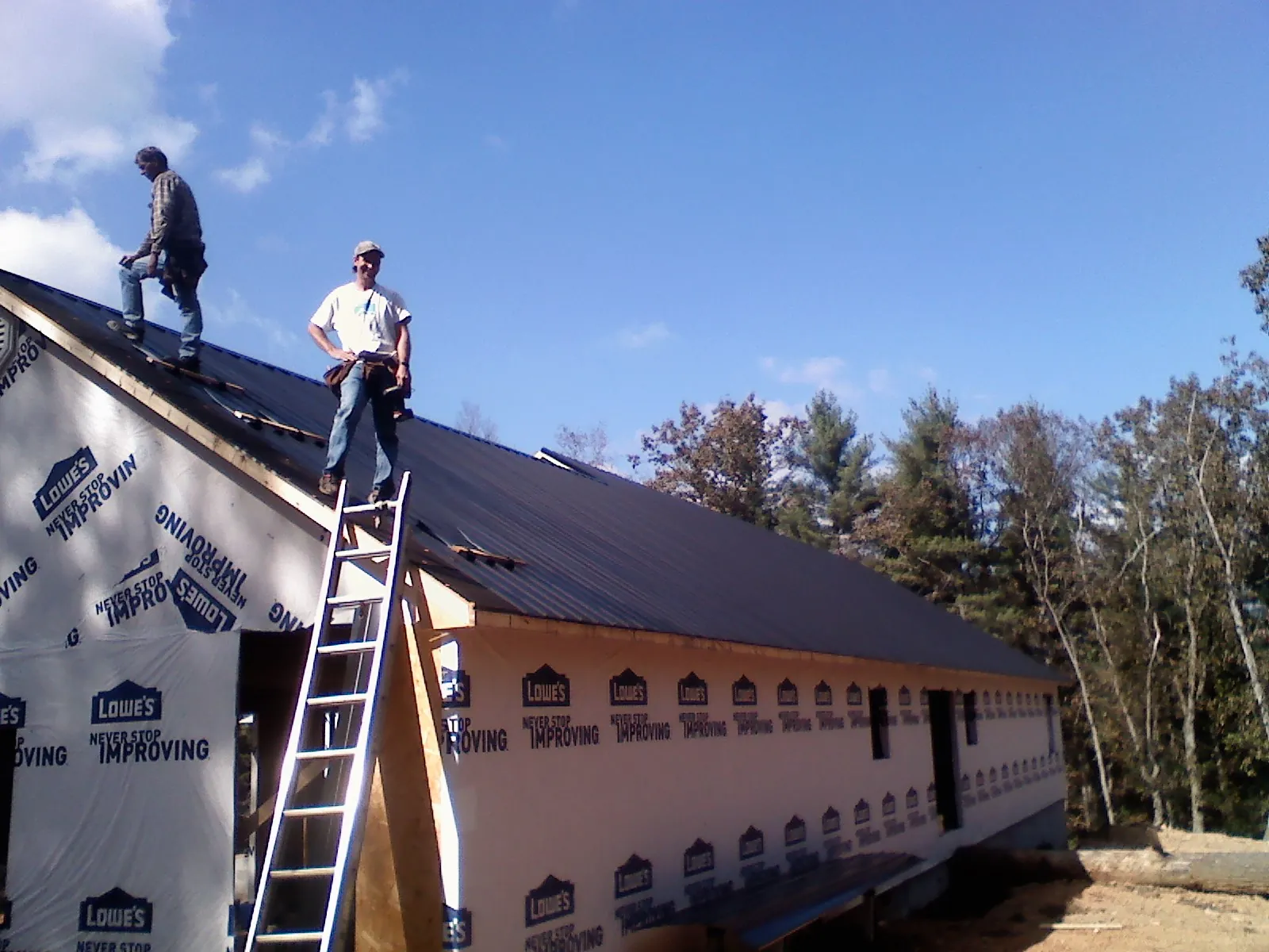 Two roofers standing on a long dark metal roof over a wrapped building in Saint John