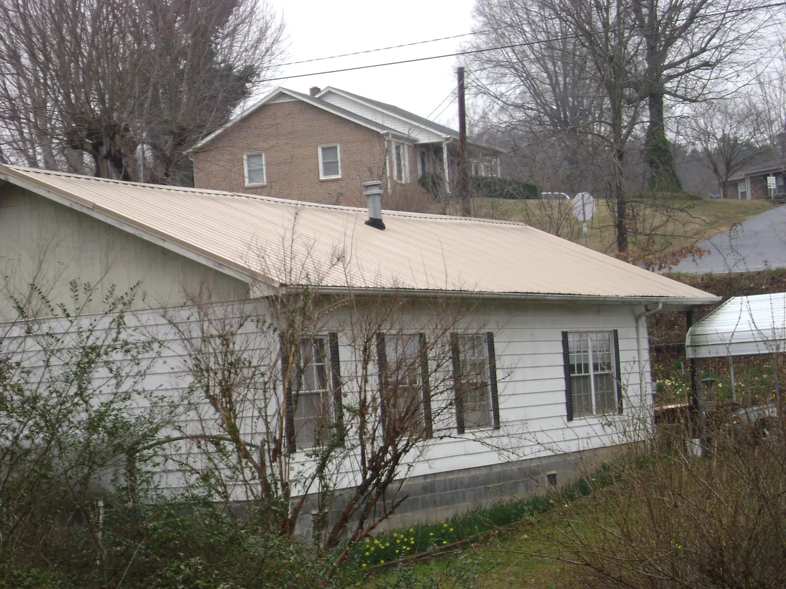 Tan metal roof on a white sided house set into a hillside — Commercial Roofing by Roofing Brothers in Saint John